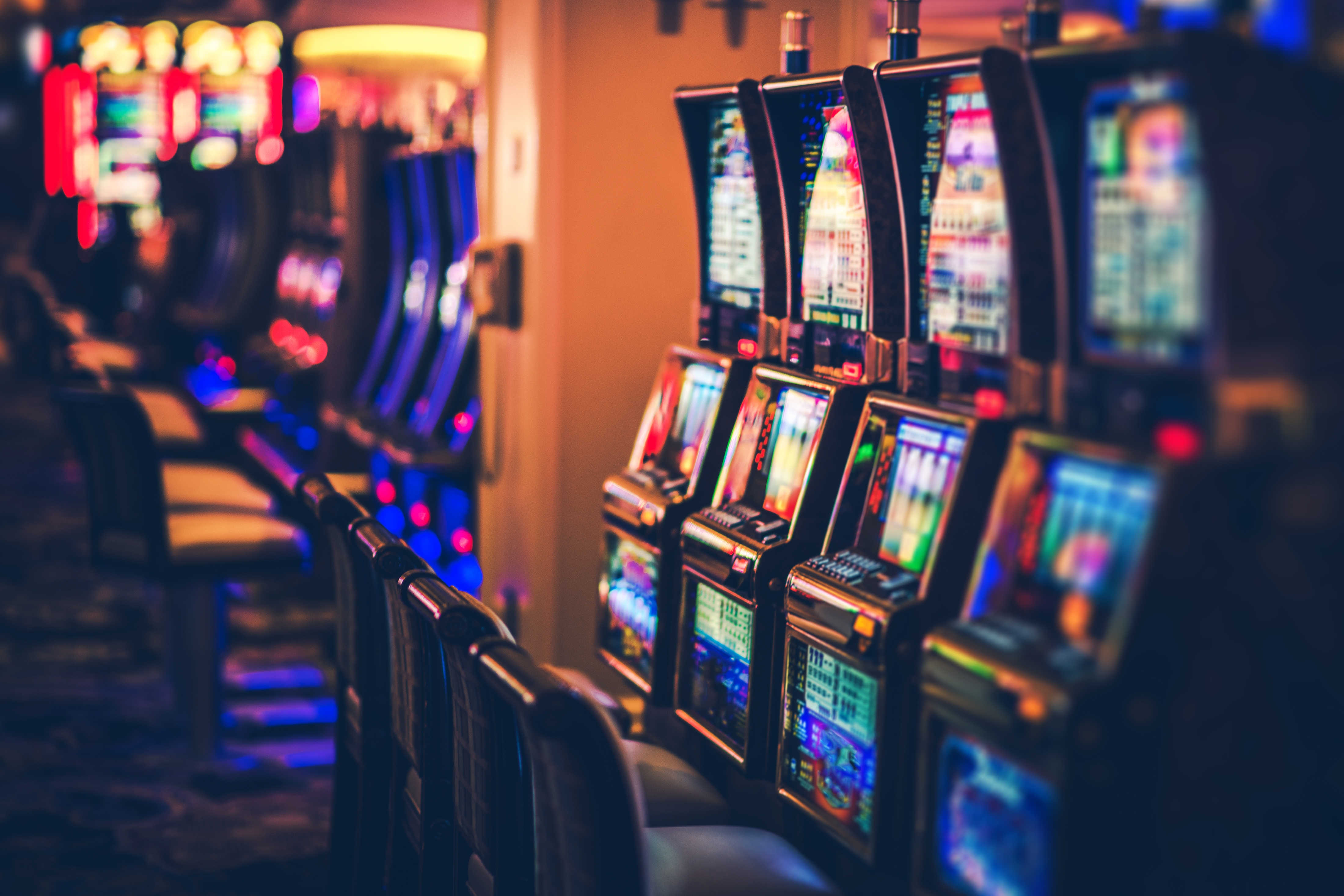 A row of glowing, colorful slot machines lined up in a darkened casino environment.
