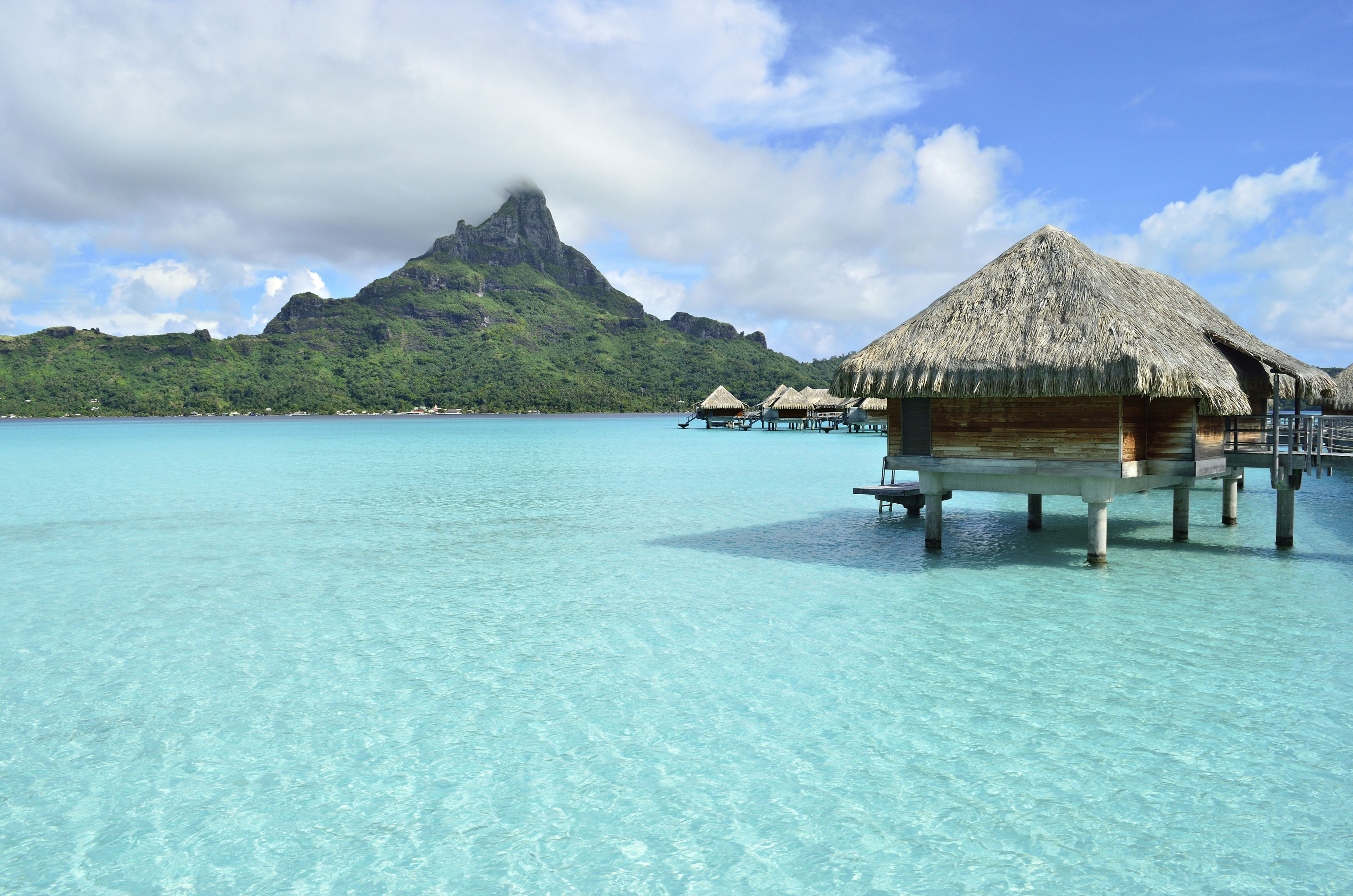Luxury bungalows perched above turquoise waters with lush forest and mountains in background