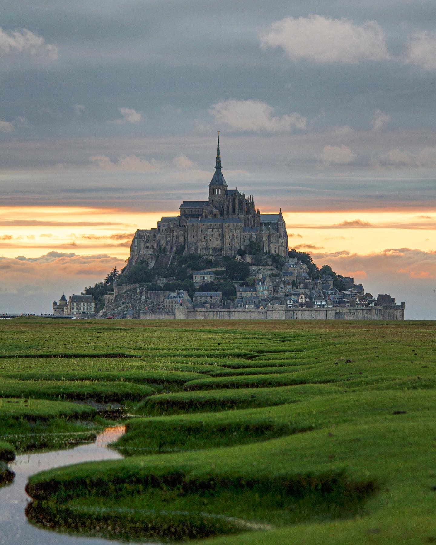 Medieval village of Mont Saint-Michel at sunset with green marshland in foreground