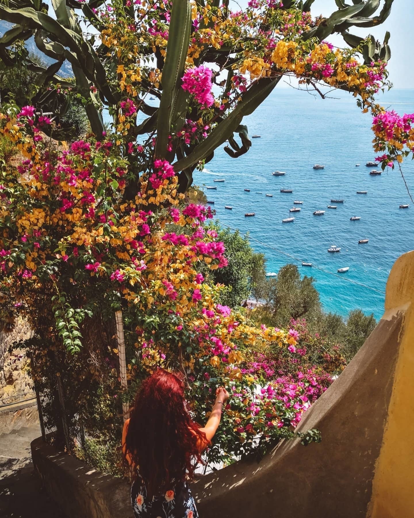Coastal view of Amalfi with woman picking bougainvillea in foreground and boats in background