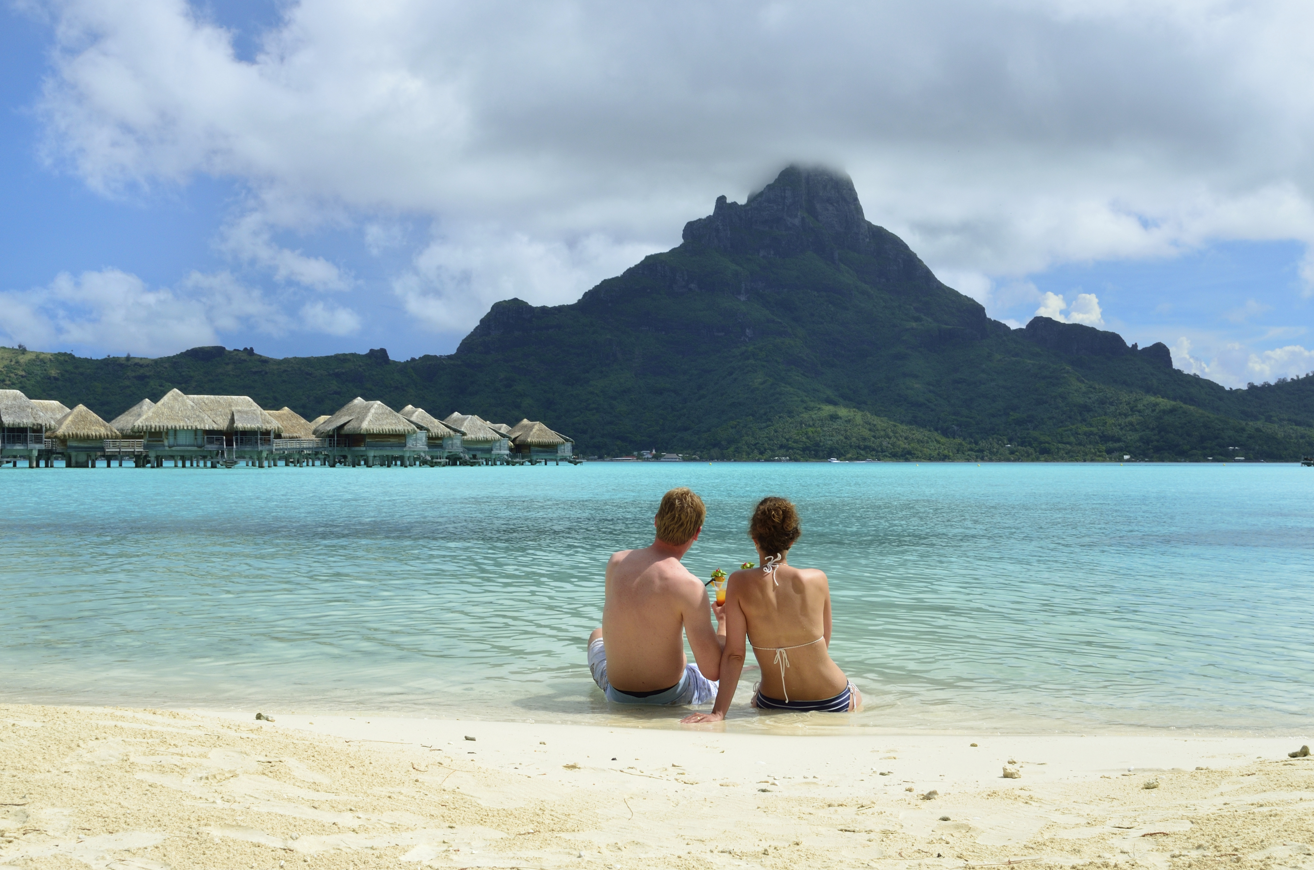 Couple sitting on beach with turquoise waters and Mount Otemanu in background