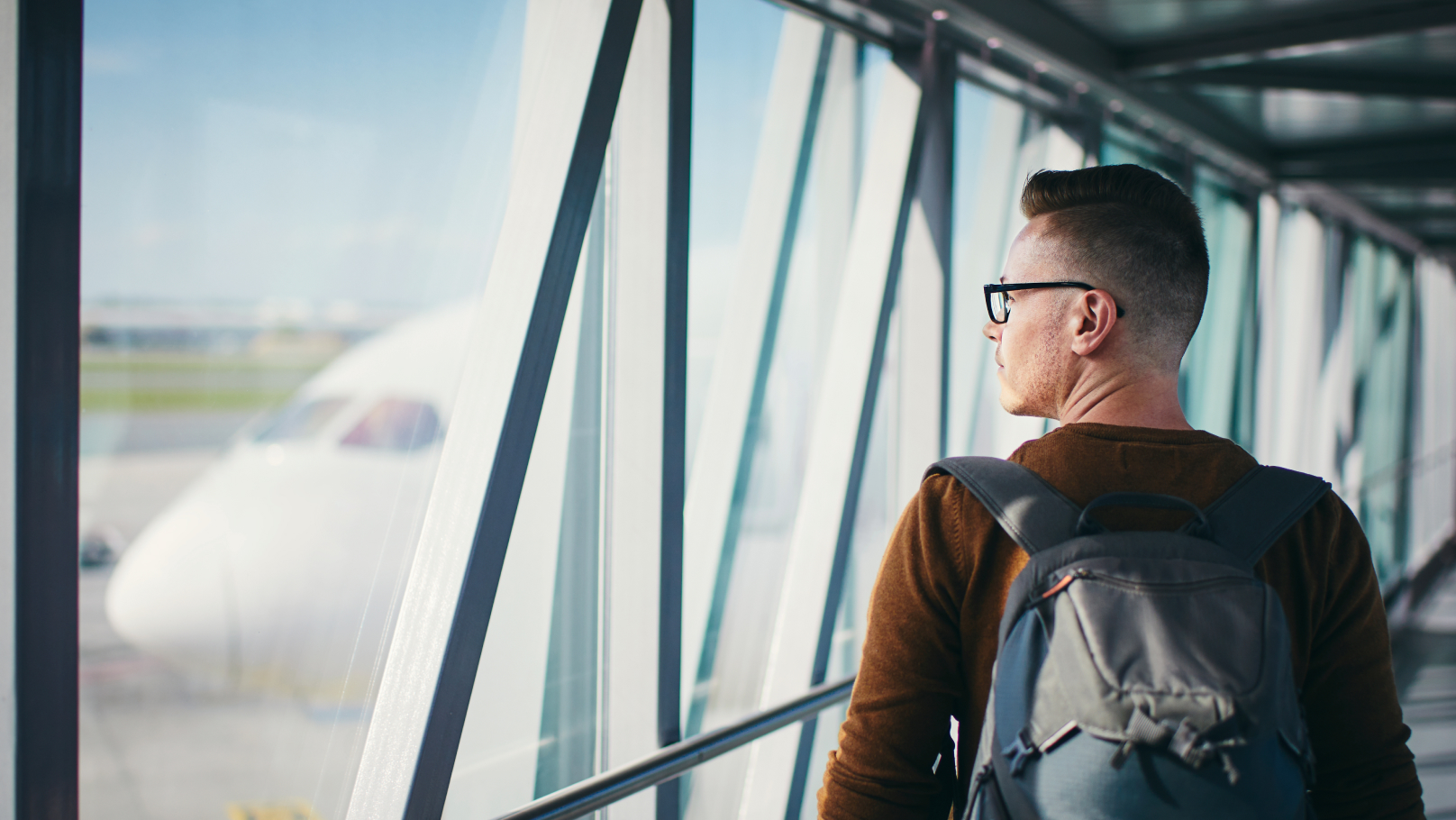 Mann am Flughafen blickt durch das Terminalfenster auf Flugzeuge am Gate.