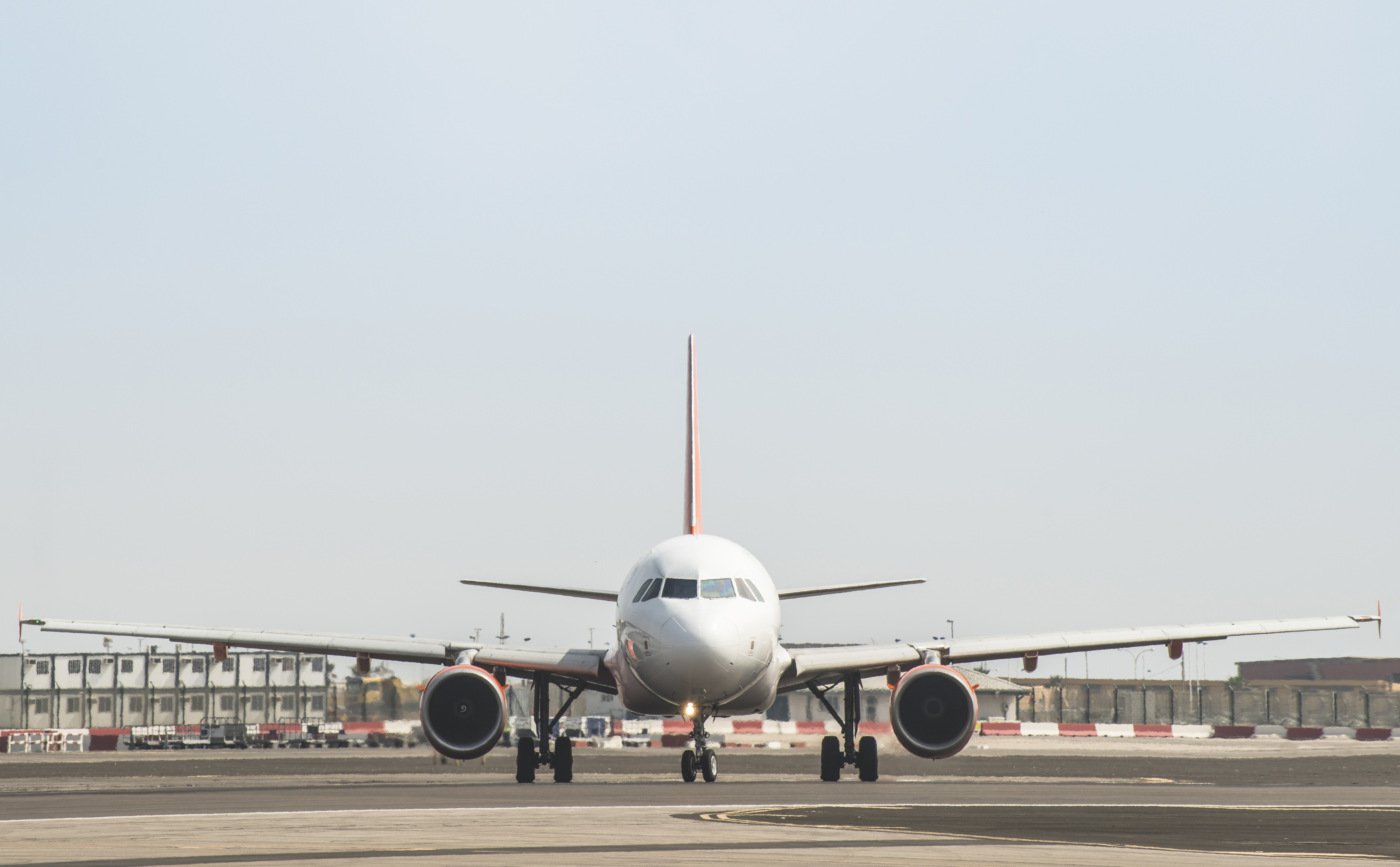 A front-facing view of a commercial passenger airplane taxiing on an airport runway under a clear sky.