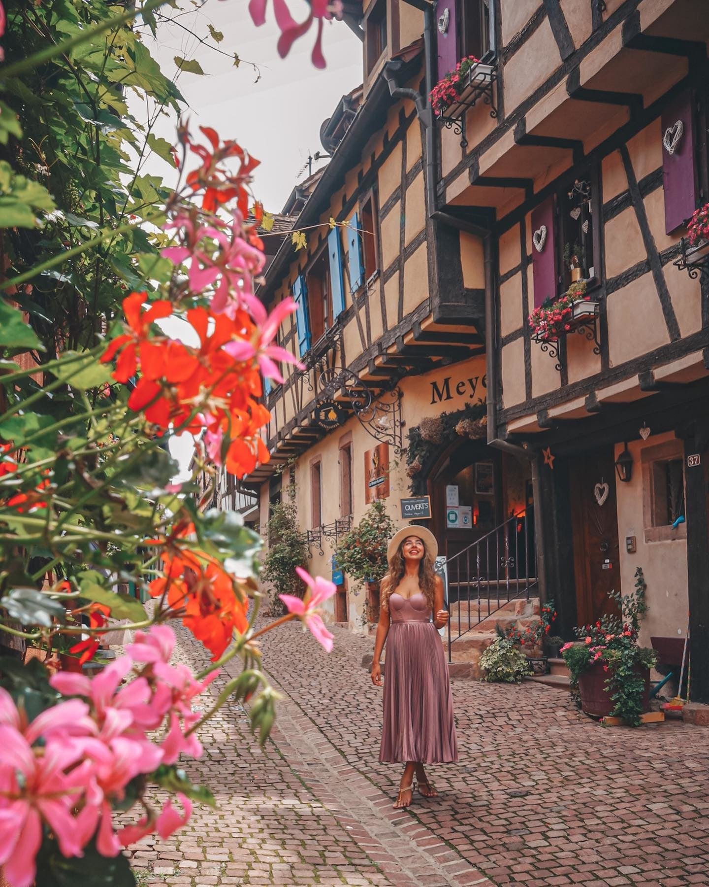 Woman in pink dress and hat walks down cobbled road in Ribeauvillé