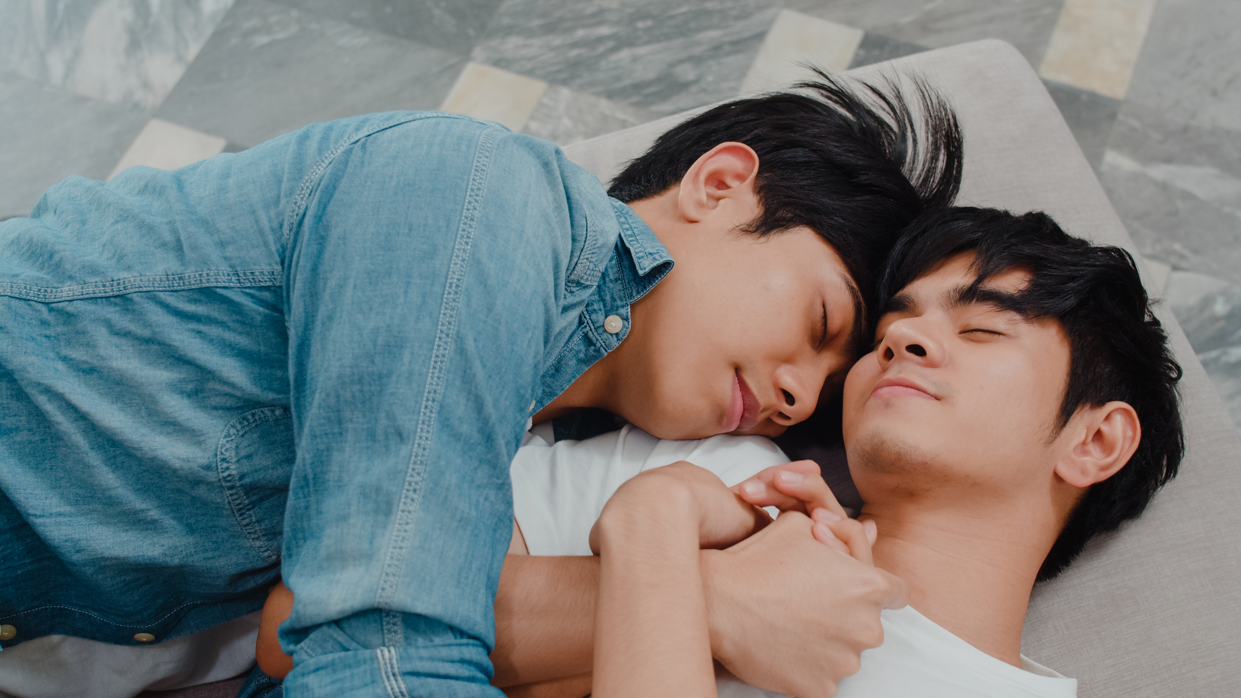 Two men hugging while lying down on the floor of a hotel room
